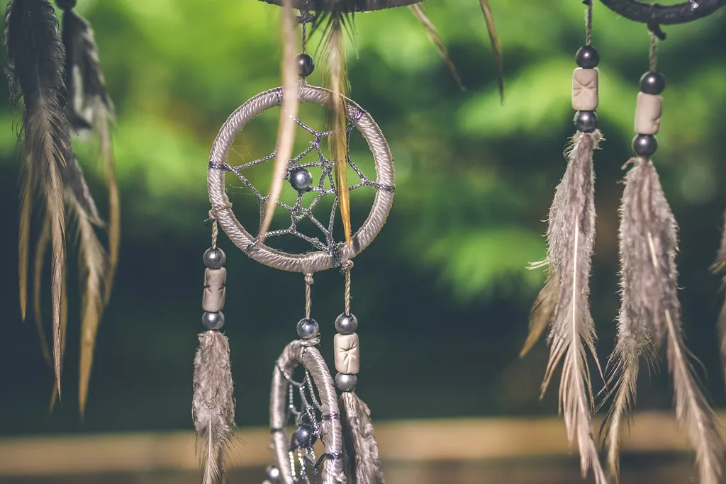 Des attrape-rêves ornés de plumes, suspendus devant un feuillage.