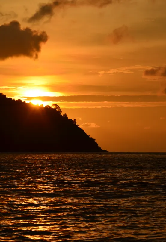 Le soleil se couche derrière une colline boisée et embrase la surface d’un lac.