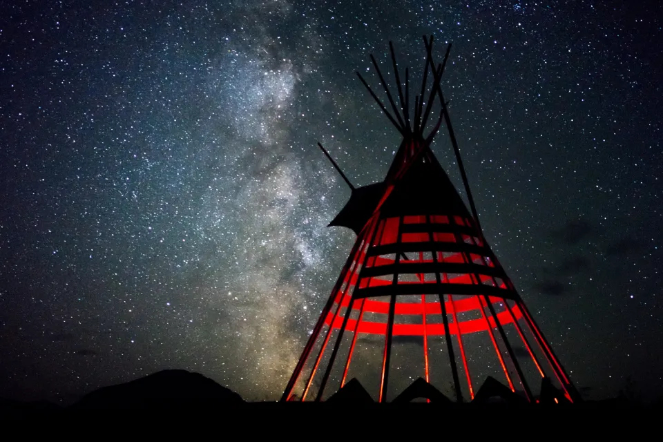 Un tipi éclairé de l’intérieur par un feu, sous la Voie lactée.